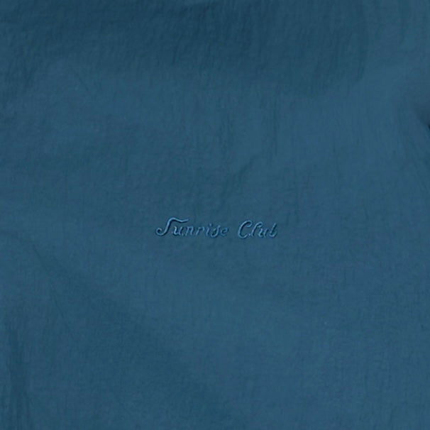 A close-up of a textured blue fabric with the words 'Sunrise Club' embroidered in a matching blue script in the center.