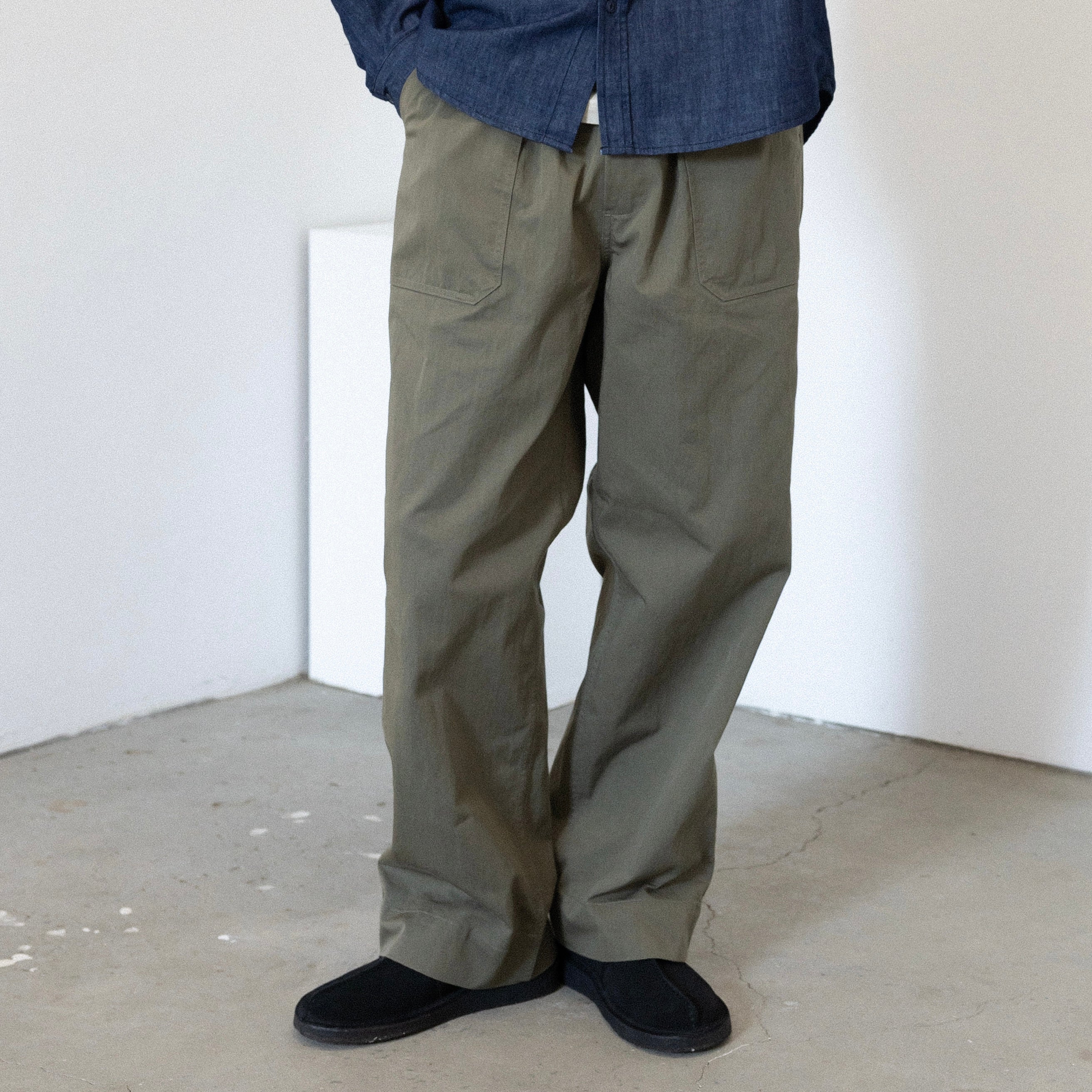 Person wearing Khaki green pants and a blue shirt in a minimalistic room.