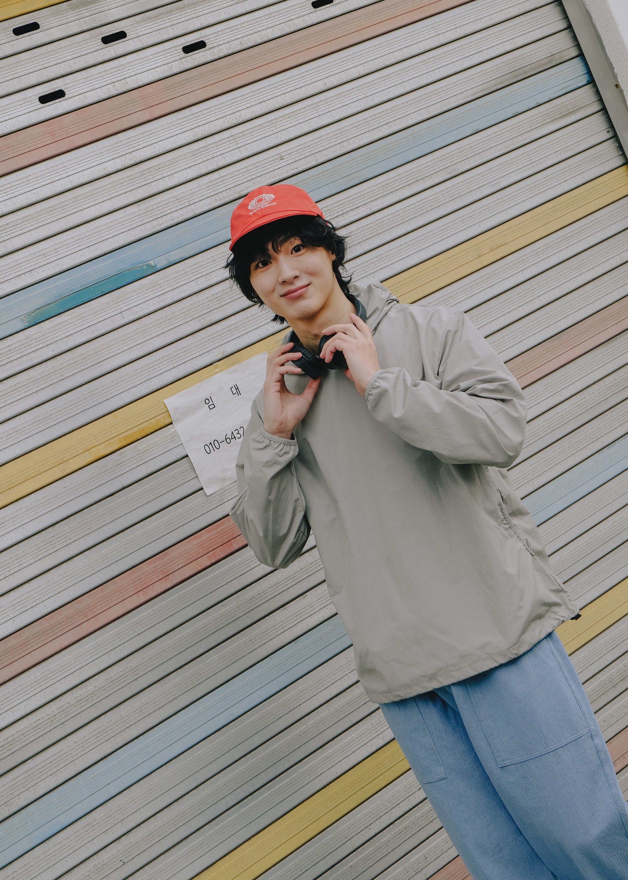 Person wearing a red cap and gray jacket against a colorful striped wall