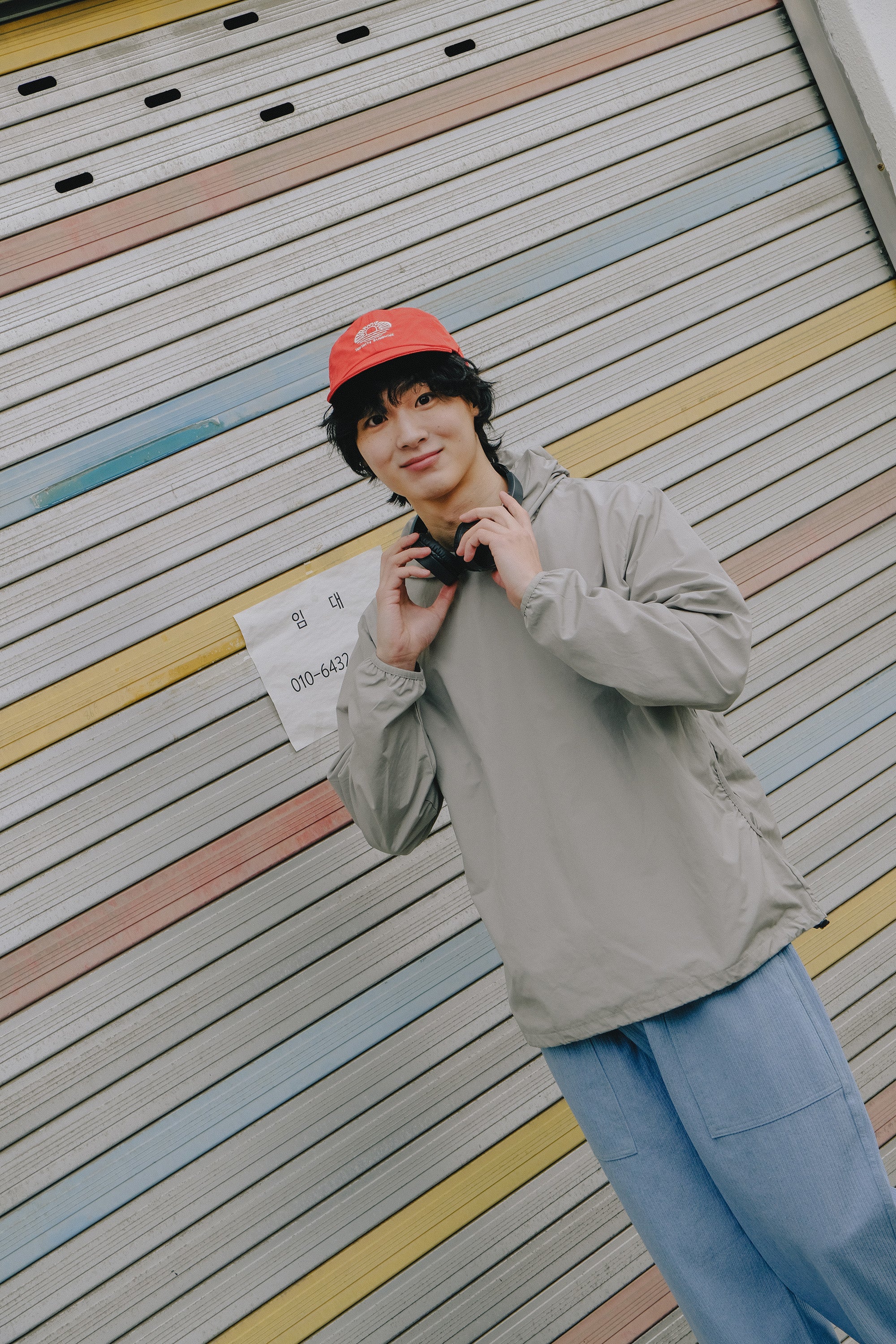 Person wearing a red cap and gray jacket against a colorful striped wall