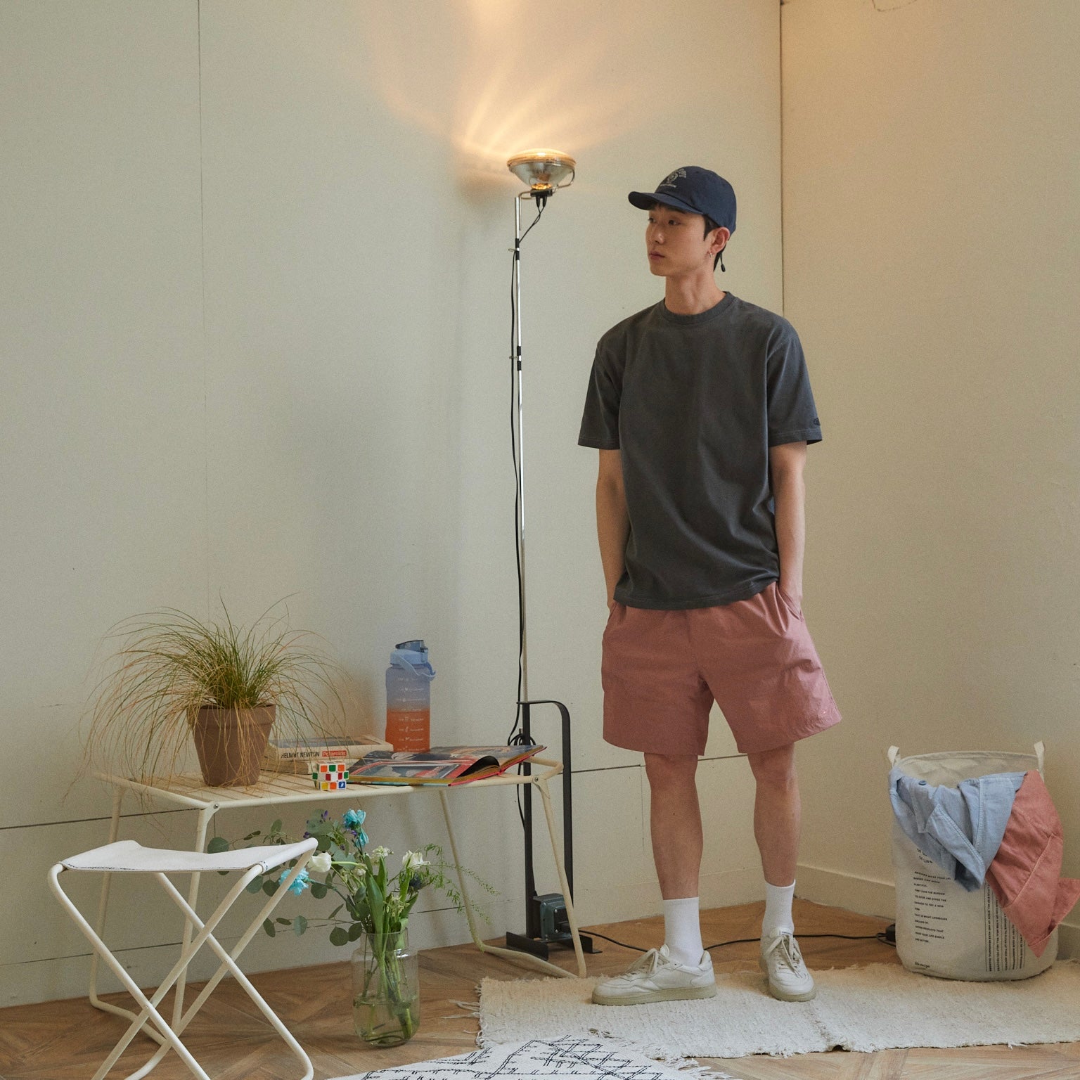 Person standing in a room with a table, lamp, and laundry basket.