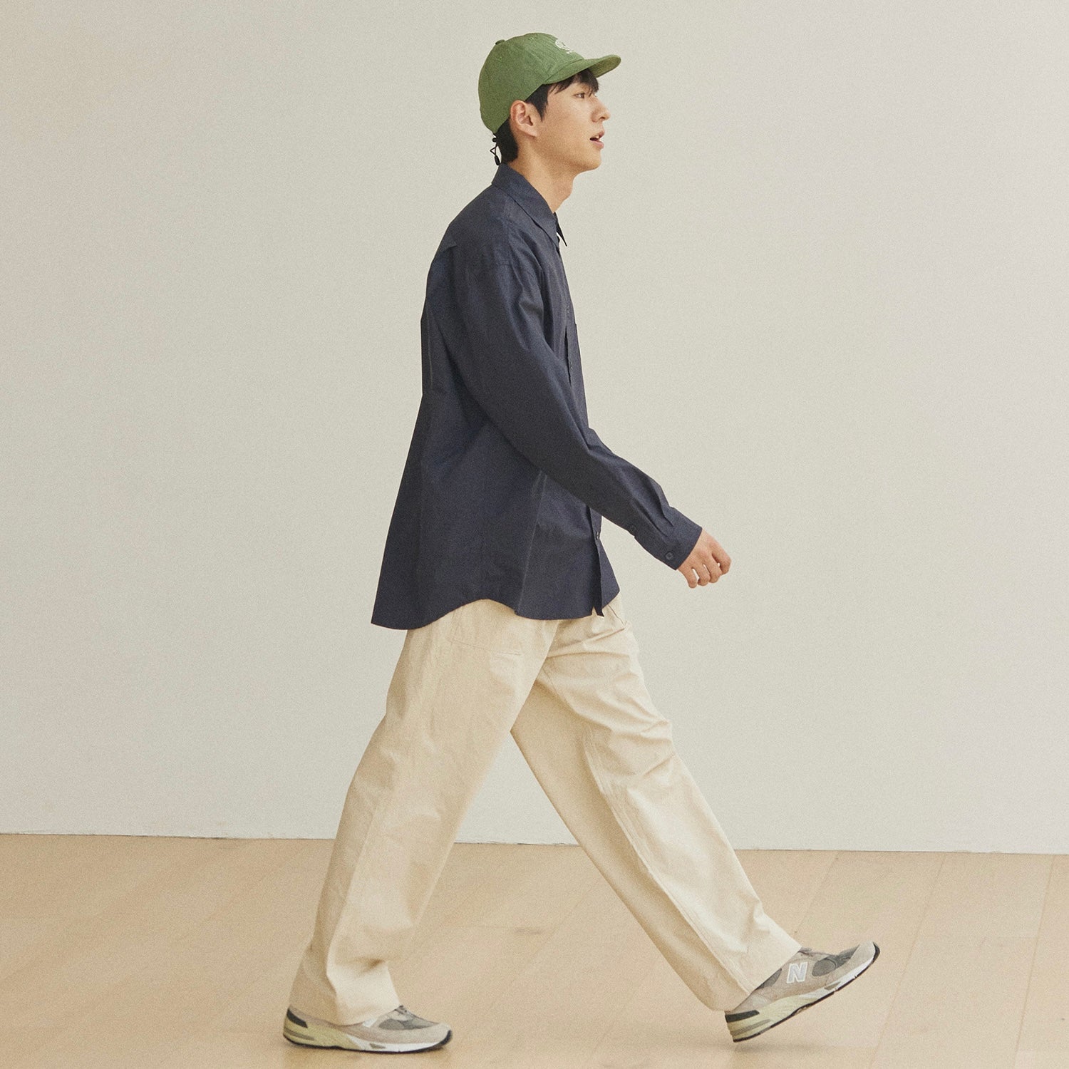 Person wearing a navy long sleeve shirt, beige pants, and a green cap on a plain background