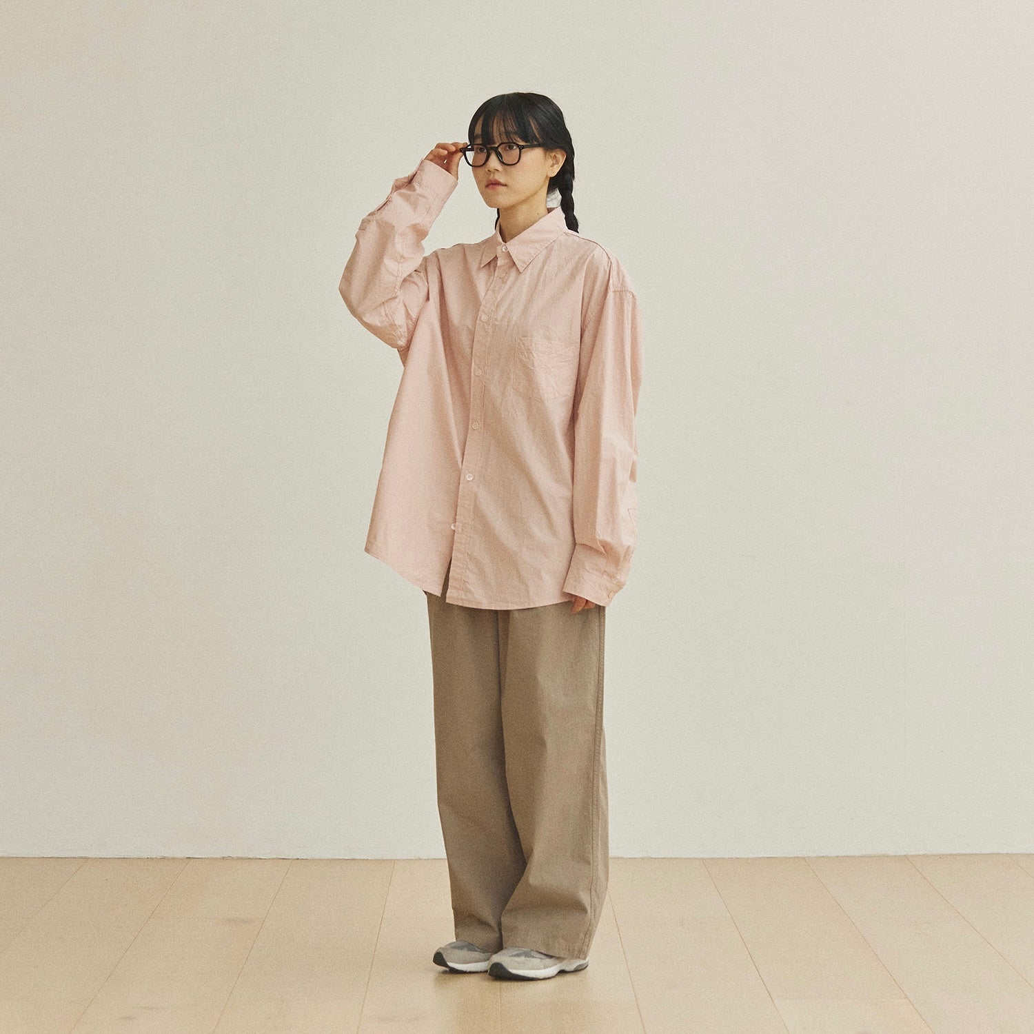 Person wearing a light pink shirt and beige pants in a minimalistic setting