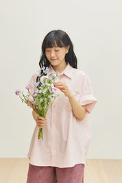 Woman in a pink short sleeve shirt holding a bouquet of flowers against a plain background