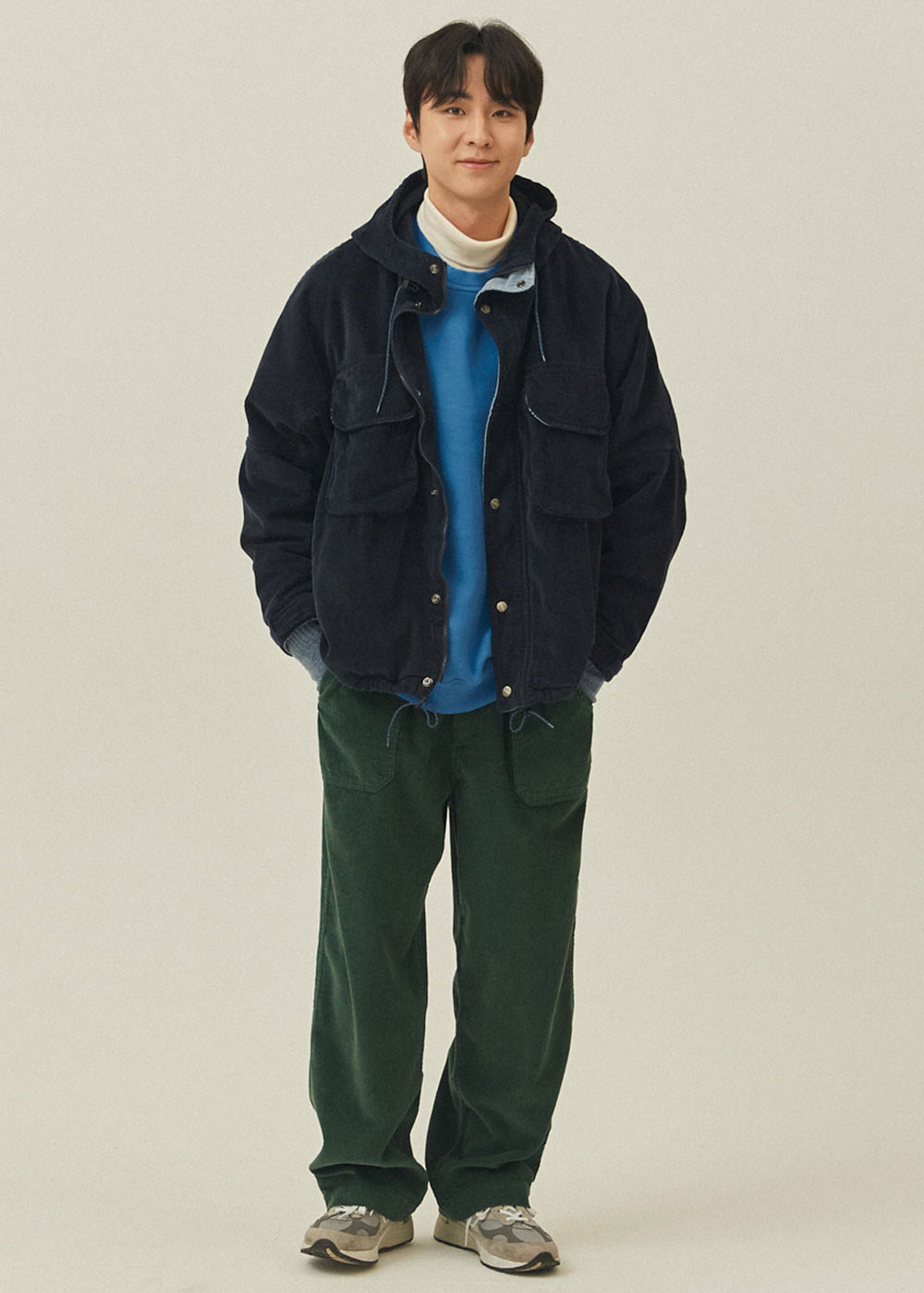Person wearing a dark jacket and green pants on a plain background
