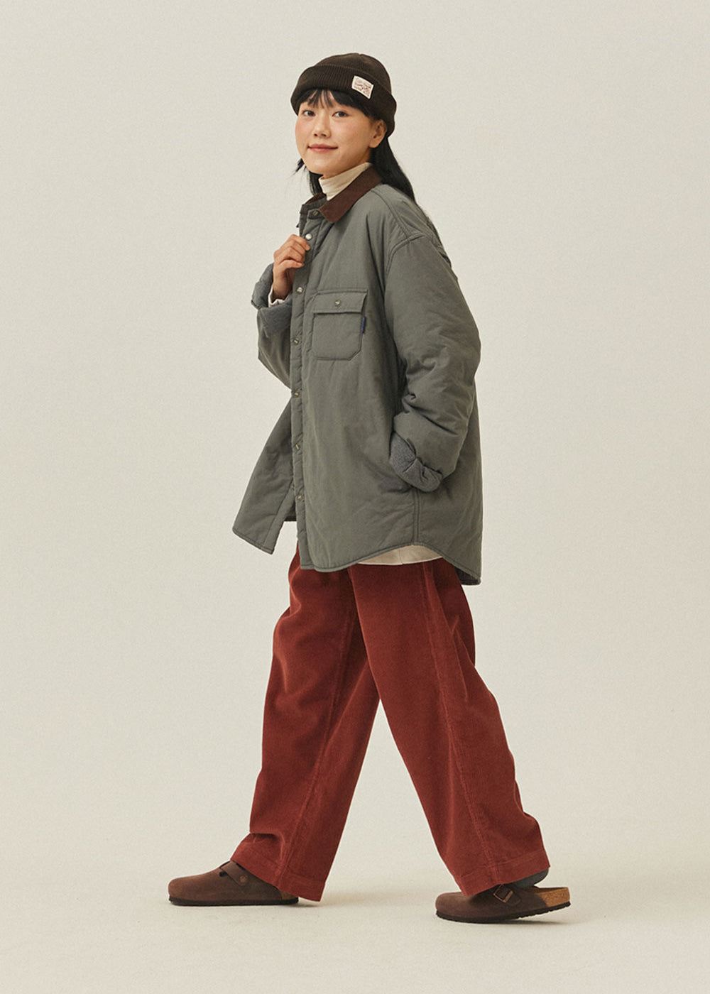 Person wearing a green jacket and red pants on a plain background