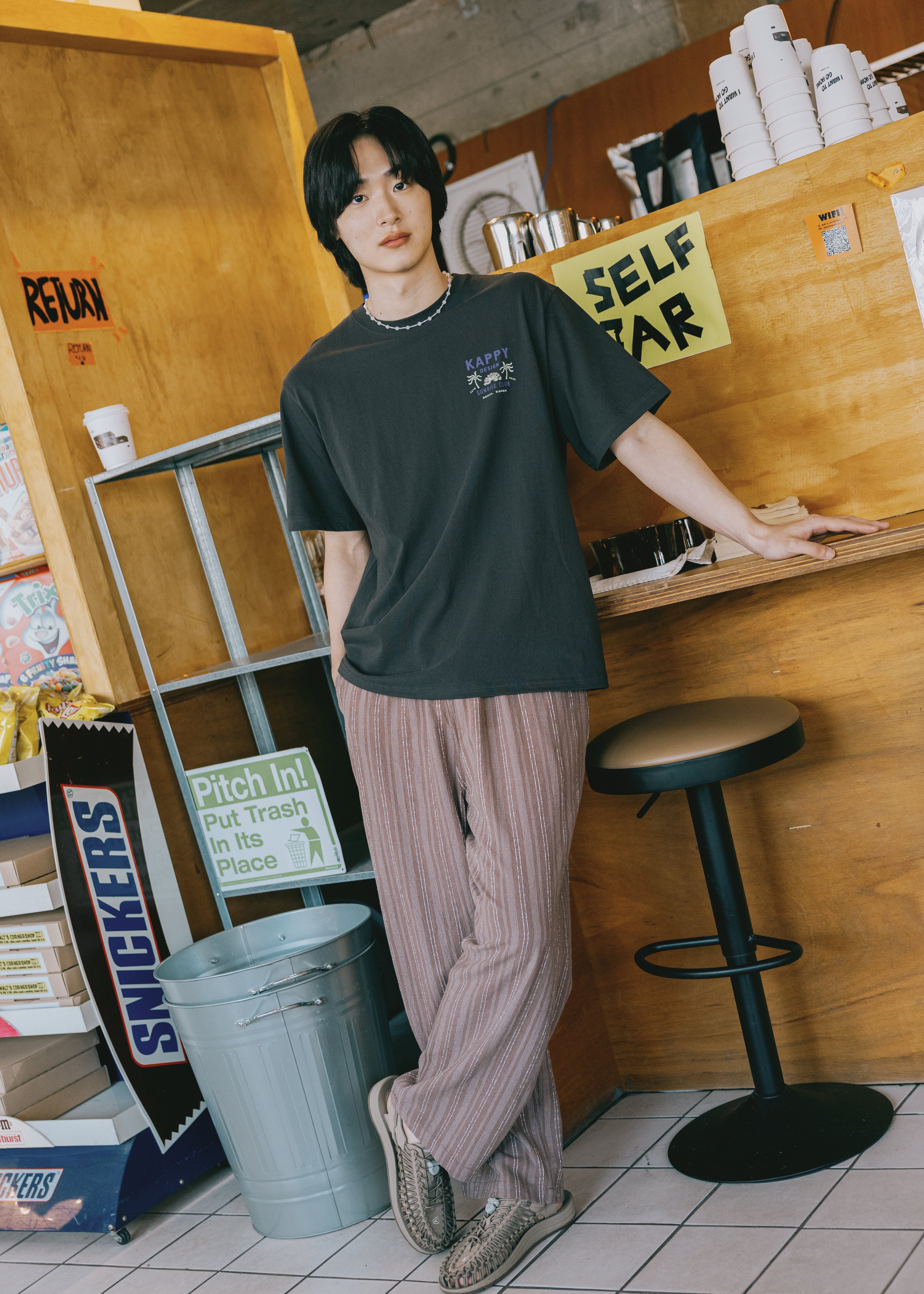 Person wearing a dark green t-shirt and light-colored pants in a casual setting.