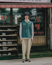 Person wearing a green vest and beige pants standing in front of a store with Korean text.