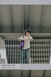 Person standing on a metal staircase with a purple bag, wearing a white shirt and green pants.