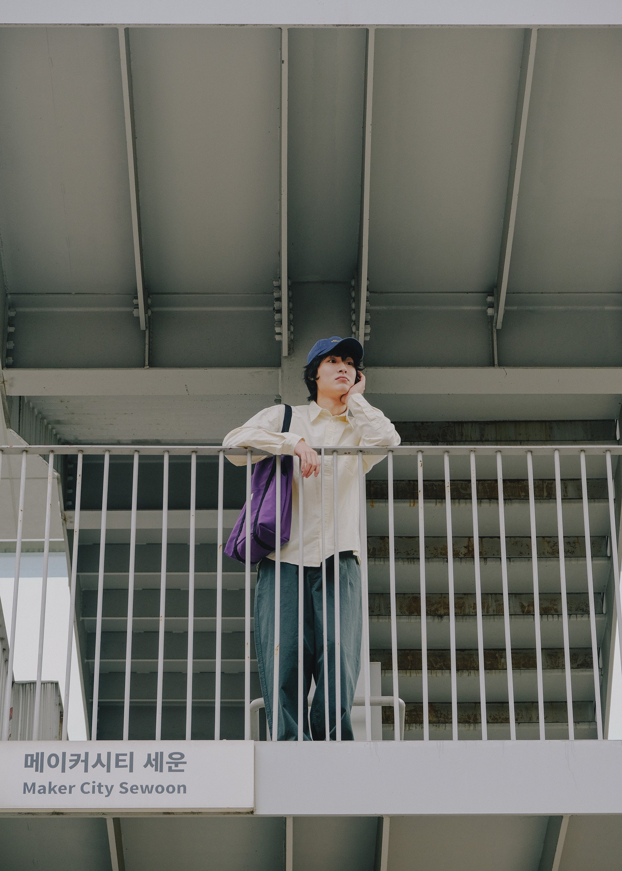 Person standing on a metal staircase with a purple bag, wearing a white shirt and green pants.