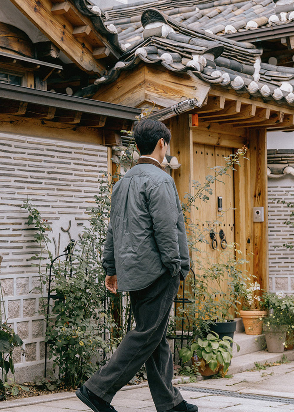 Man walking past a traditional wooden house with tiled roof