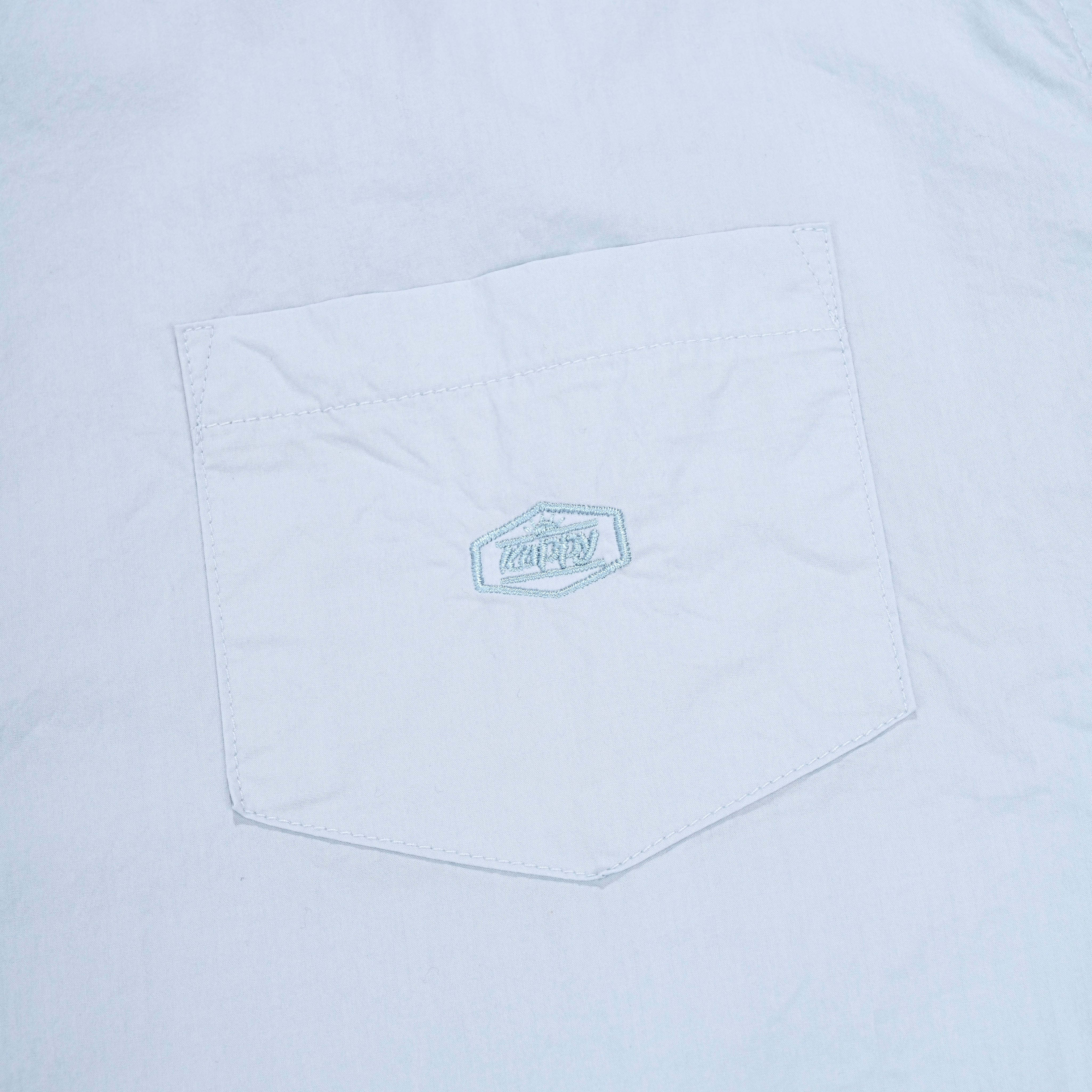 Close-up of a light blue pocket on a shirt with a logo.