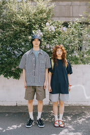 Two people standing outdoors with greenery and a building in the background