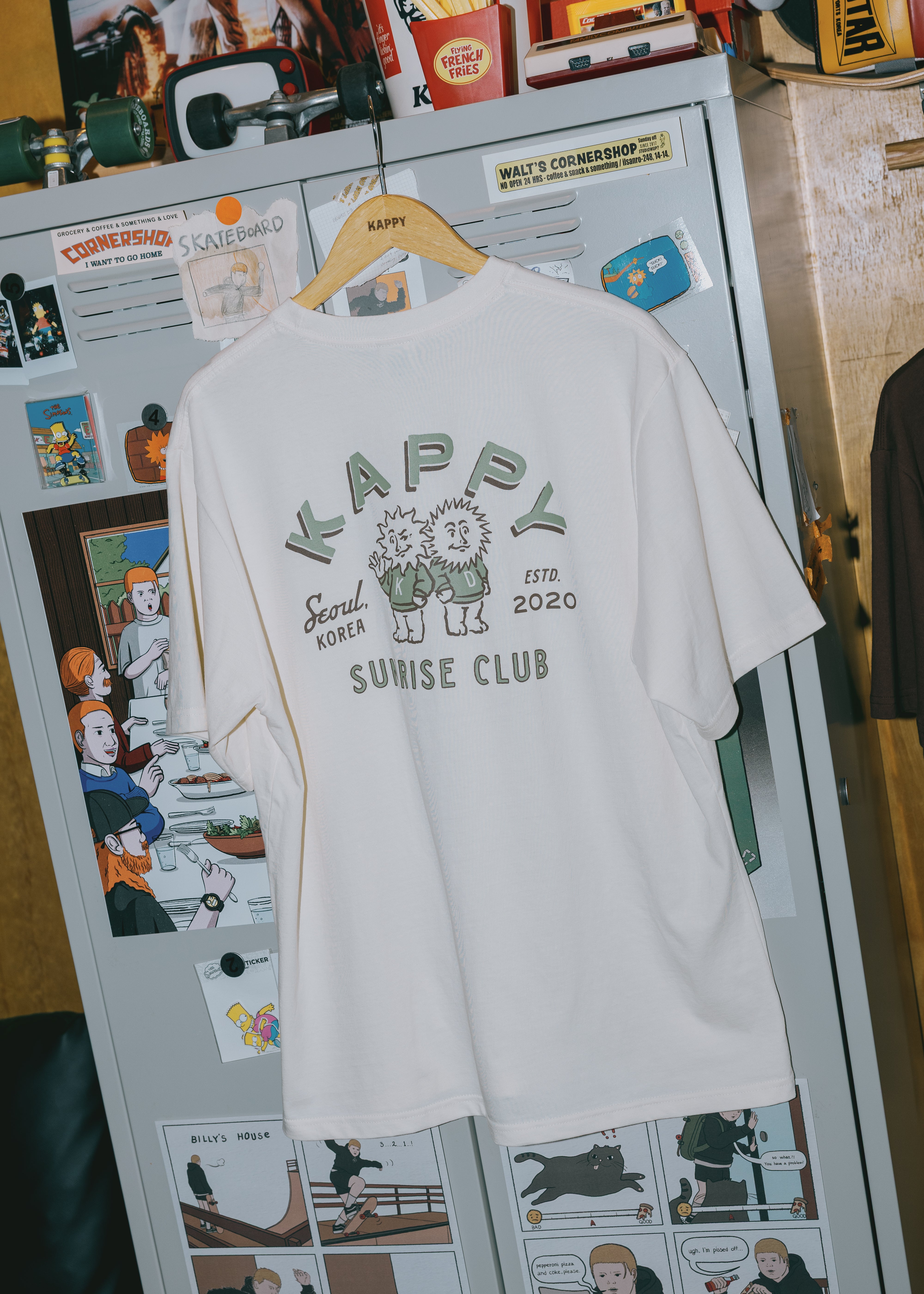 cream t-shirt with graphic design on a refrigerator with magnets and photos.