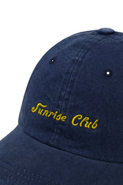 Close up of Navy blue cap with 'Sunrise Club' embroidered in yellow on a white background