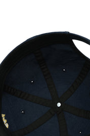 Close-up of a navy blue cap with black strap and white stud on a white background