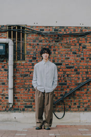 Person standing against a brick wall wearing a striped shirt and brown pants.