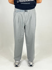 Person wearing grey pants and a black shirt with visible branding on a white background
