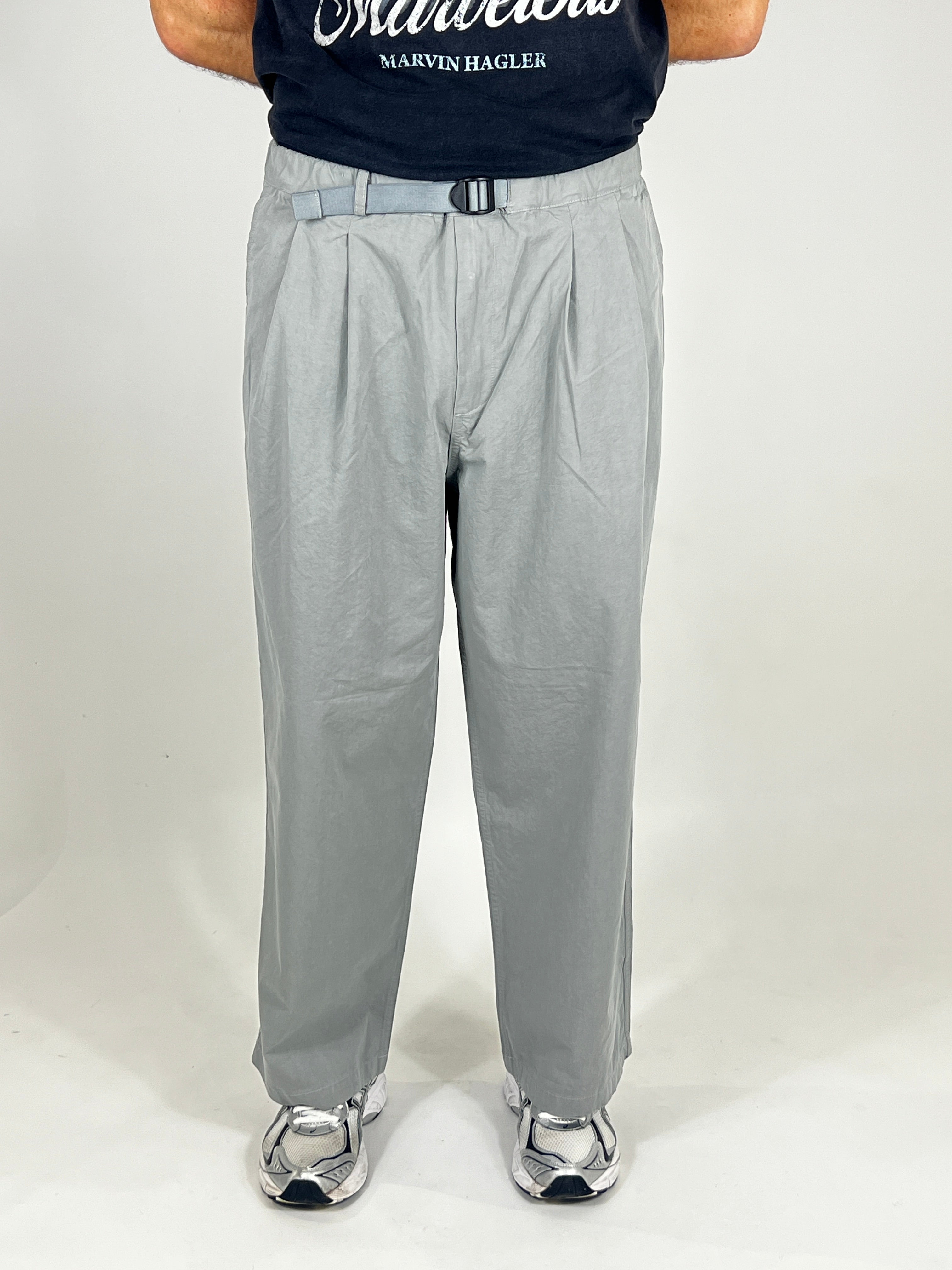 Person wearing grey pants and a black shirt with visible branding on a white background