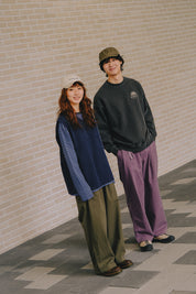 Two people standing against a brick wall, wearing casual clothing.