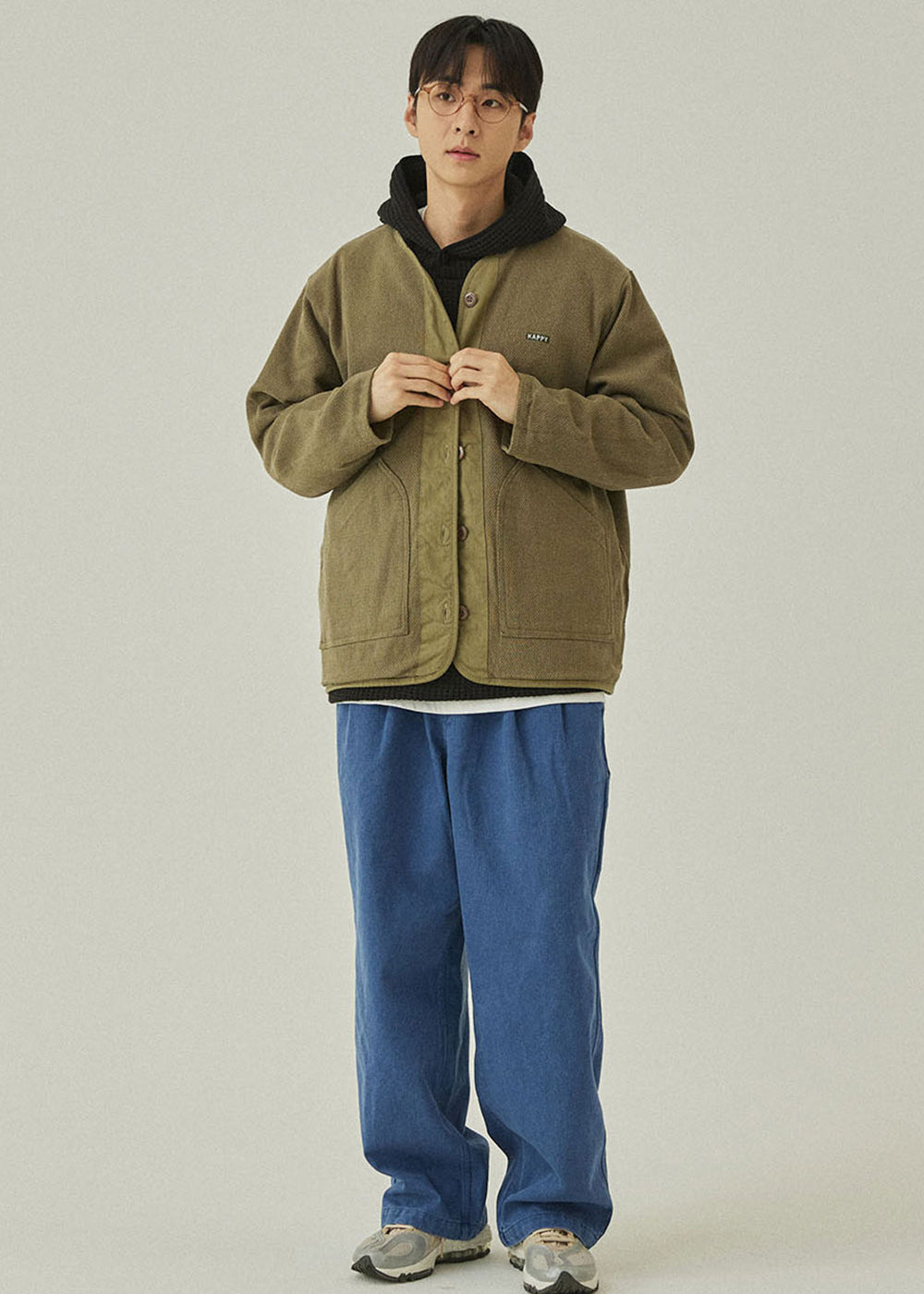 Person wearing a green jacket and blue pants on a plain background