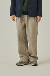 Person wearing a navy jacket, green shirt, beige pants, and gray shoes on a plain background