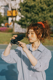 Person holding a camera outdoors with greenery in the background