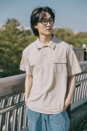 Person wearing a beige shirt and blue jeans standing outdoors with trees in the background